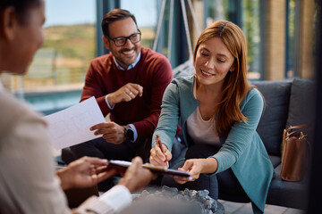 Happy couple signing contract on meeting with real estate agent.