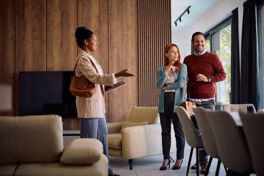 Black real estate agent showing new house to happy couple during open house day.