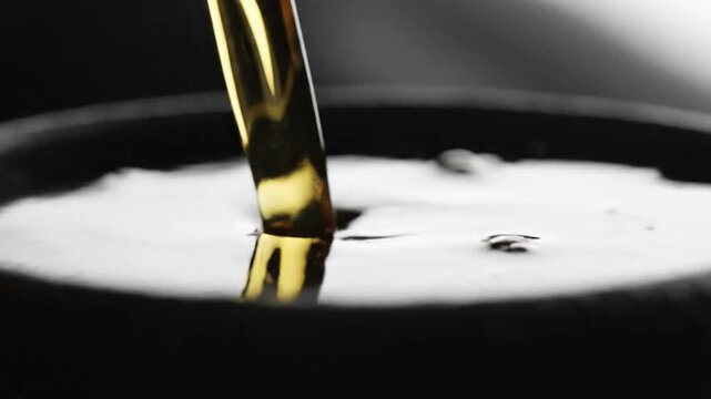Close-up of golden liquid pouring into a bowl with a dark background and dramatic lighting.