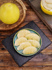 Fresh White Pomelo Citrus Fruit Slices in Bowl with Whole Fruit on Rustic Wood Table