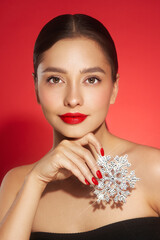 Beautiful young woman with red lipstick, shiny clean skin and face, showing glowing snowflake, near face and smiling, isolated on a red background. Christmas holidays concept