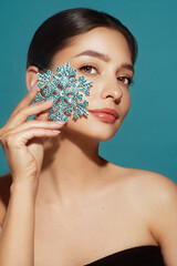 Beautiful young woman with red lipstick, shiny clean skin and face, showing glowing snowflake, near face and smiling, isolated on a blue background. Christmas holidays concept