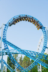 Roller coaster Ride against blue sky. Roller coaster in the amusement park. Cheerful entertainments in park of attractions