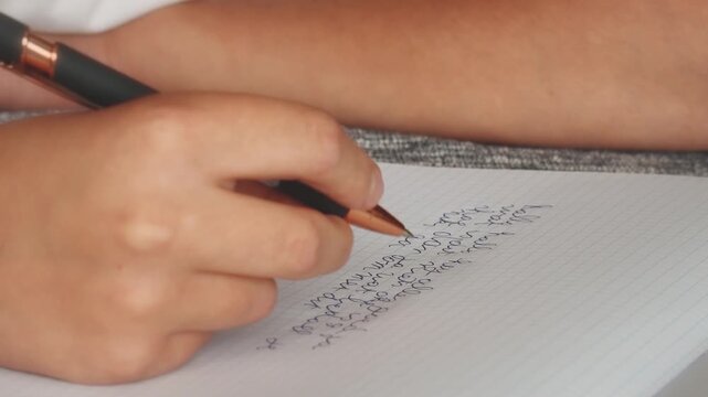 Teenager practices writing with a pen on notebook paper at home during afternoon study session