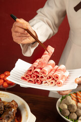 Chef Preparing Sliced Raw Meat Rolls with Chopsticks for Hot Pot Cooking