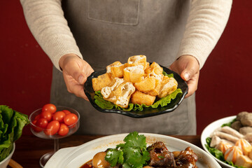 Asian woman serving crispy fried tofu cubes with vegetables and fresh ingredients for healthy cooking