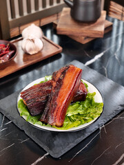 Wood-fired smoked bacon strips on plate with lettuce garnish in rustic kitchen