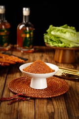 Spicy red chili powder in bowl with Asian cooking ingredients on rustic wooden table