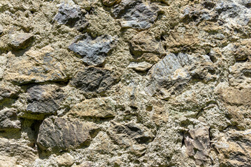 The masonry of an antique wall made of rough dark stones bonded with light mortar