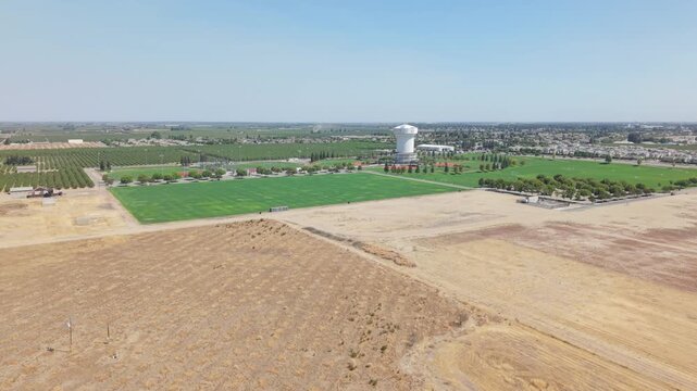 Aerial tracking shot moving over farmland toward water tower and city in Ripon California.