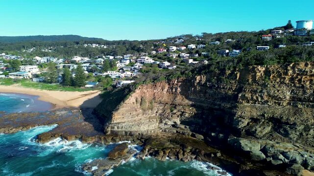 Drone aerial landscape pan around North Avoca rocky headland cliffs with surrounding bushland trees and residential housing along scenic coastline Central Coast NSW Australia nature tourism travel
