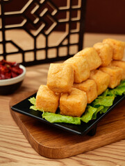 Golden Fried Tofu Cubes on Black Plate with Lettuce Garnish - Traditional Asian Cuisine