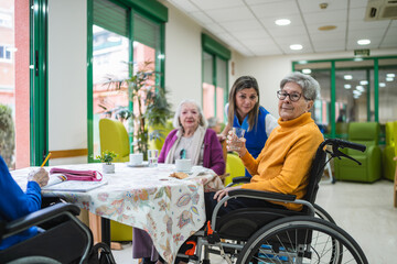 Senior women socializing at a table in an assisted living facility with a caregiver providing support and assistance