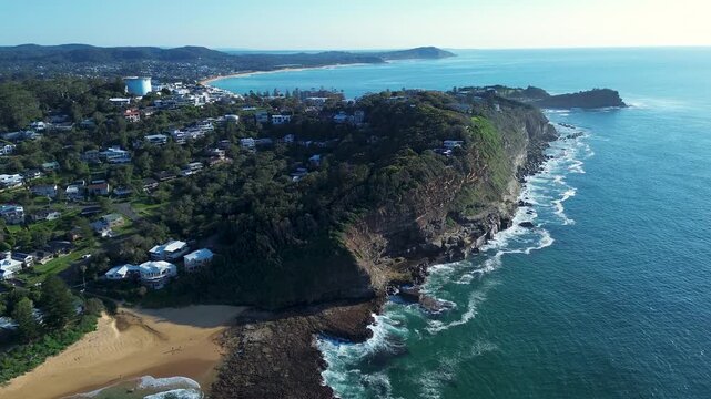 Drone aerial landscape of North Avoca beach bushland cliffs and coastal rural headland with residential homes on the street and a water tower in background Terrigal Central Coast Australia holidays