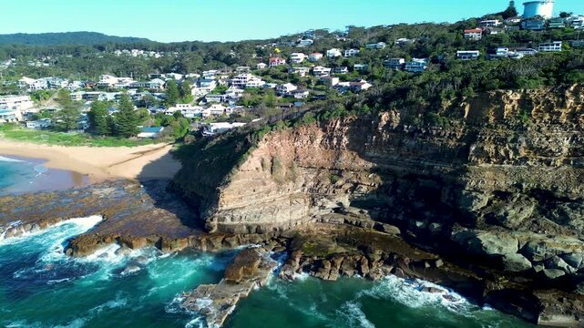 Drone aerial landscape of rugged headland cliffs at North Avoca Beach with ocean reef clear blue water and residential homes stretching along scenic coastline on Central Coast region Australia tourism