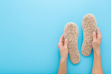 Young adult woman hands holding and showing new light soft natural sheep wool insoles on light blue table background. Pastel color. Closeup. Empty place for text. Point of view shot. Top down view. © fotoduets