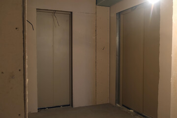Two elevators passenger and cargo in entrance of apartment building under construction. Cement rough repairs during renovation. Finishing works in hall of multi-storey house.