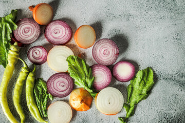 Top view of fresh sliced onions, hot green peppers and greens on light concrete background. Natural light, rustic style, organic autumn harvest, clean eating mood