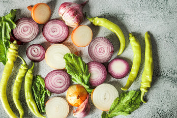 Top view of fresh sliced onions, hot green peppers and greens on light concrete background. Natural light, rustic style, organic autumn harvest, clean eating mood