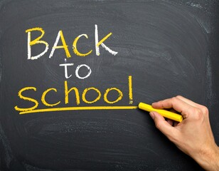 'Back to school' written in white and yellow chalk on a dark blackboard, with a hand underlining "school" in yellow