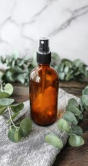 Amber glass spray bottle with a black spray top, sitting on a gray linen cloth, surrounded by eucalyptus leaves on a dark wooden surface