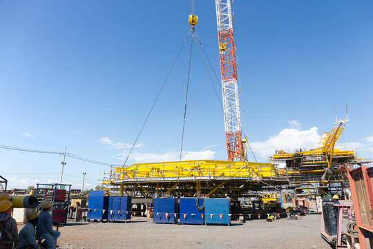 Crane lifting large industrial component of oil drilling rig against blue sky. Steel truss boom of crawler crane hoists heavy load with sling during oil and gas construction project.