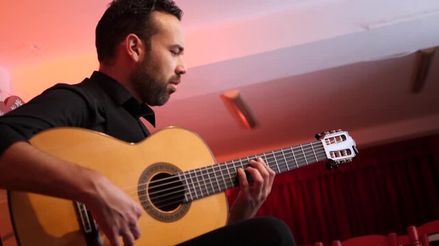Focused male musician playing a traditional Spanish guitar in a tablao. The artist performs a flamenco melody with skill and concentration