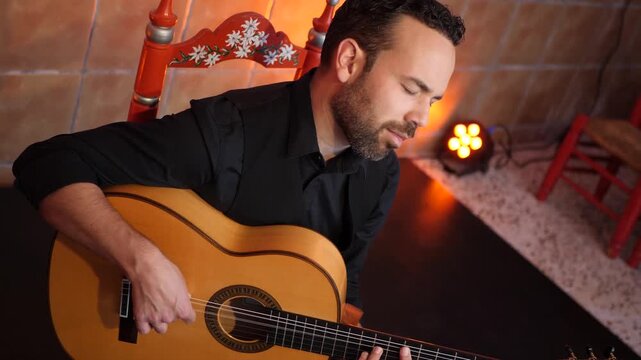 Male musician playing a traditional Spanish guitar in a tablao. The guitarist passionately performs a flamenco melody during a live concert