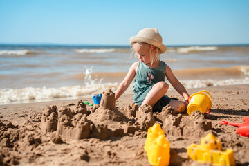 Cute little child girl makes a sand castle with molds on the beach in summer