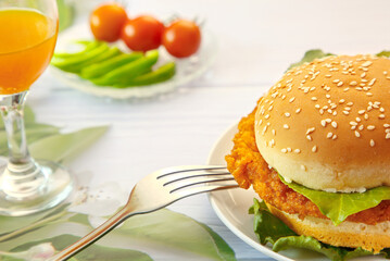 Close-up hamburger, orange juice, tomatoes, fork on white table, depth of field