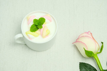 Close-up, milk with marshmallow and mint, pink rose on cloth pattern background