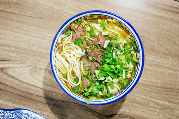 Close-up beef noodle with clear soup on wooden table, minced garlic, beef slices