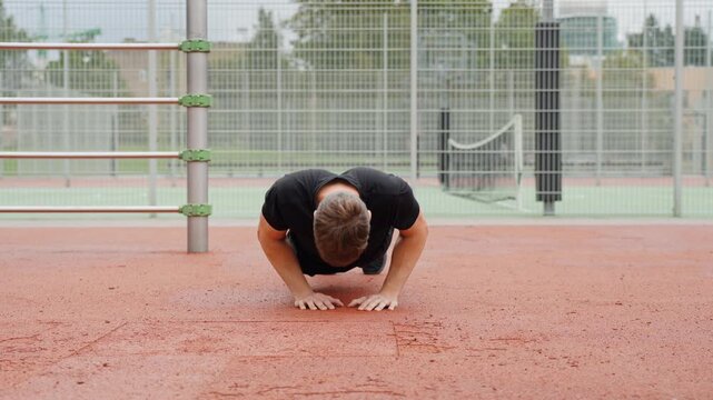 Young man doing push ups on a red outdoor court, engaging in intense calisthenics training and building strength for a healthy lifestyle, low static camera, slow motion