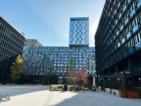 Modern glass office courtyard with tall buildings Novotel Wien Hauptbahnhof and outdoor seating in an urban plaza in Vienna, Austria.