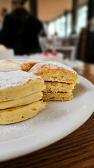Close-up of delicious melt butter cream sugar powder with raspberry banana fruit pearl pancake triple layers on a wooden table in a stylish elegant Ginza Tokyo café, winter afternoon tea atmosphere