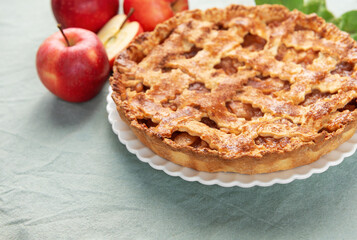 Freshly baked apple pie with red apples and leaves on green tablecloth