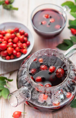 Steaming rosehip tea brewing in glass teapot with fresh rosehips