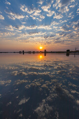 A stunning sunrise over calm water with clouds beautifully reflected on the surface.