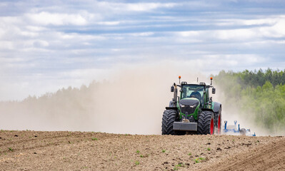 Obraz premium A tractor in a field plows the ground at dawn, sowing grain. High quality photo. green tractor plowing cereal field with sky with clouds