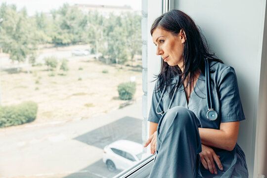 Nurse with stethoscope in uniform resting by window reflecting on work life