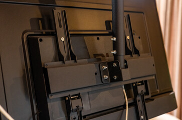 Swivel TV bracket LED display. Side view. X-shaped red fasteners. Black color. Multiplanar. Hangs on a wall. Reliable and comfortable fastening. Childproof and rollover protection. Metallic equipment.