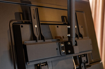 Swivel TV bracket LED display. Side view. X-shaped red fasteners. Black color. Multiplanar. Hangs on a wall. Reliable and comfortable fastening. Childproof and rollover protection. Metallic equipment.