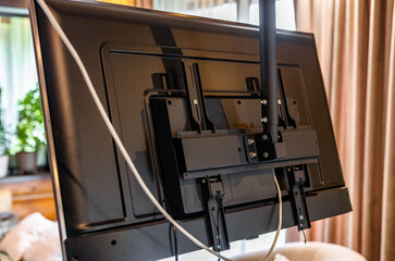 Swivel TV bracket LED display. Side view. X-shaped red fasteners. Black color. Multiplanar. Hangs on a wall. Reliable and comfortable fastening. Childproof and rollover protection. Metallic equipment.