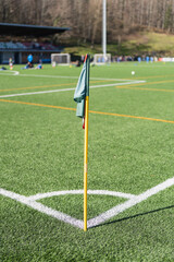 Soccer corner flag stands on a bright green field during a sunny day in a sports complex