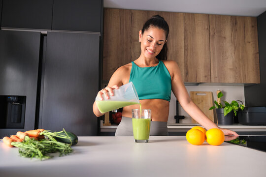 Woman in activewear making green smoothie in modern kitchen