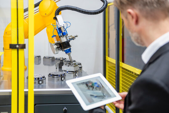 Engineer monitoring industrial robot arm in modern factory with tablet