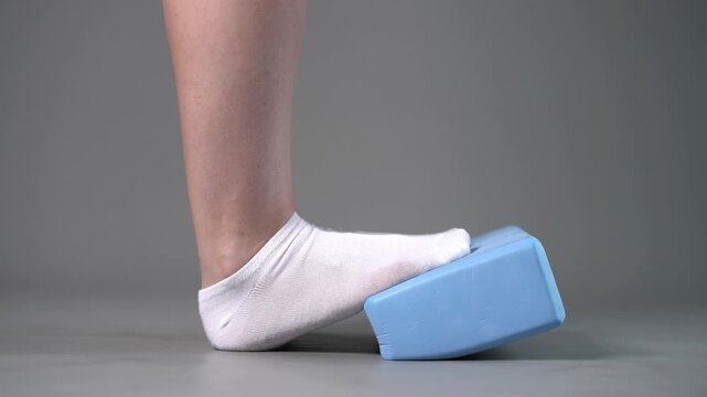 Individual balance training on a blue block with bare feet, demonstrating foot position and stability on a gray studio background