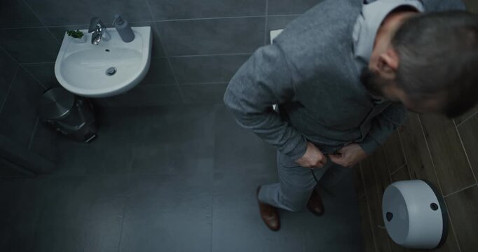 Man Entering in Restroom, Sitting on the Toilet and Suffering from Diarrhea and Stomach Ache. Businessman Experiencing Digestive Discomfort and Indigestion During Work in Modern Office. High Angle.