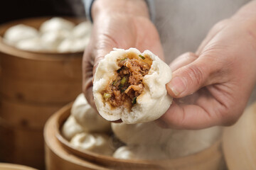 Traditional Chinese Bao Steamed Bun with Meat Filling Held in Hand Over Bamboo Steamer Basket
