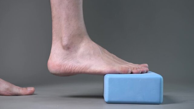 Individual balance training on a blue block with bare feet, demonstrating foot position and stability on a gray studio background
